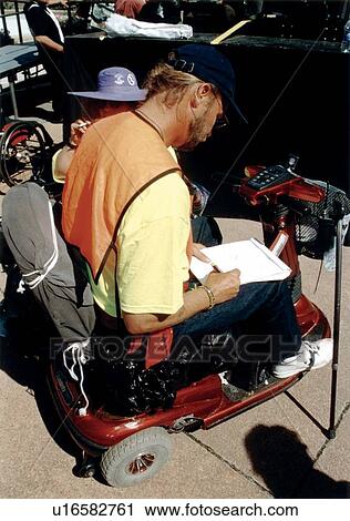 Stock Image - Man with a disability utilizing a cart/scooter for mobility taking notes while attending the ADAPT March on Washington event to advocate for the civil rights of people with disabilities.. Fotosearch