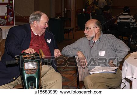 Man with a disability, utilizing a scooter for mobility, talking with a participant at a conference. View Large Photo Image Stock Photo - Man with a disability, utilizing a scooter for mobility, talking with a participant at a conference.. Fotosearch