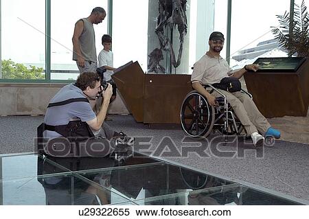 Stock Photography - Man with a disability, utilizing a wheelchair for mobility, posing for the camera at an exhibit.. Fotosearch