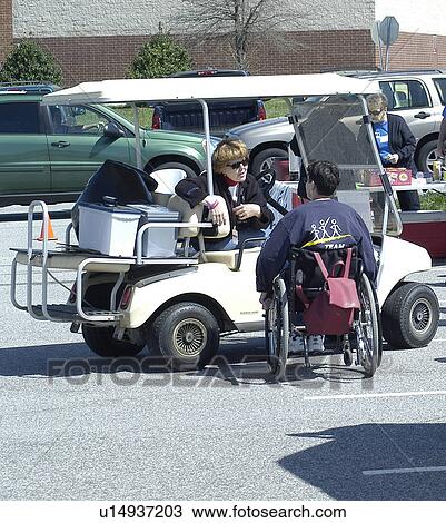 Stock Image - Woman in golf cart and woman in wheelchair visit at a community event. Fotosearch