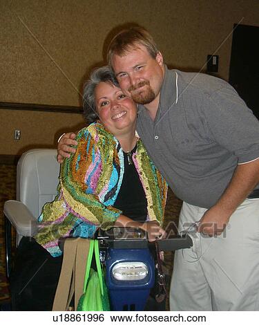 Stock Photograph - Woman in wheelchair receives a hug from a friend who has a developmental disability.. Fotosearch
