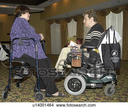 Woman with a disability, utilizing a scooter for mobility, talking with a woman with a disability who is resting on her walker which ôdoublesö as a resting seat. View Large Photo Image Picture - Woman with a disability, utilizing a scooter for mobility, talking with a woman with a disability who is resting on her walker which ôdoublesö as a resting seat.. Fotosearch