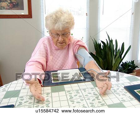 Stock Image - An elderly woman looks at her reading after taking a blood pressure reading.. Fotosearch