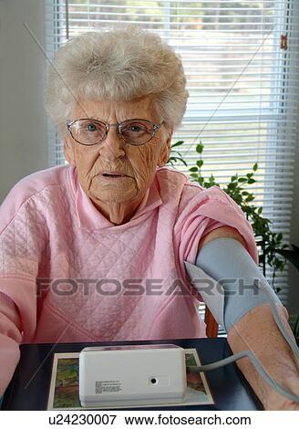 An elderly woman looks forward while taking a blood pressure reading. View Large Photo Image Stock Photo - An elderly woman looks forward while taking a blood pressure reading.. Fotosearch