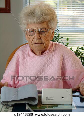 Stock Photograph - An elderly woman prepares for a blood pressure reading.. Fotosearch