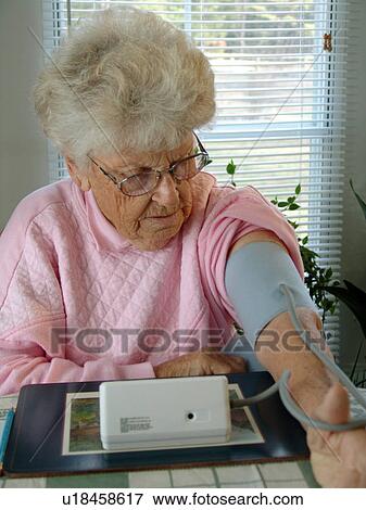 An elderly woman straps on blood pressure cuff. View Large Photo Image Stock Photo - An elderly woman straps on blood pressure cuff.. Fotosearch