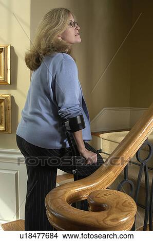 Picture - Lady with arm crutches walks upstairs.. Fotosearch