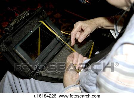 Stock Photograph - Woman with cerebral palsy, sitting in a wheelchair typing on speech devise while holding a strap to balance the equipment on her lap.. Fotosearch