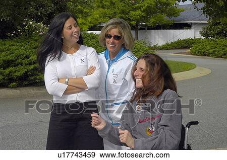 Stock Photo - A young woman with physical disabilities smiling and laughing with two female friends on a street outside of a suburban home.. Fotosearch