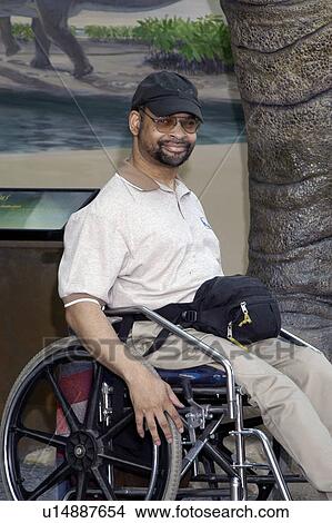 Man with a disability, utilizing a wheelchair for mobility, smiling and posing for the camera. View Large Photo Image Picture - Man with a disability, utilizing a wheelchair for mobility, smiling and posing for the camera.. Fotosearch