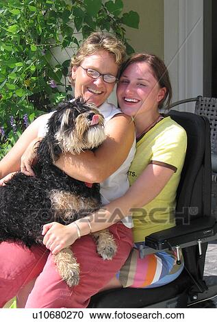Stock Image - Mother and pet dog share a ride with daughter using an electric wheelchair.. Fotosearch