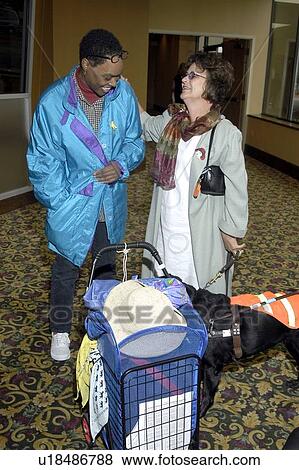 Stock Photo - Two individuals with visual impairments/blindness talking and exchanging tips during a break at an assistive technology conference.. Fotosearch