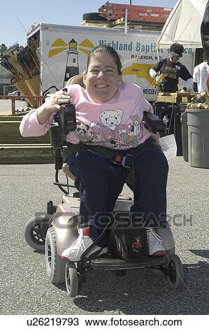 Stock Image - Woman in a power wheelchair moving toward the camera at a community event. Fotosearch