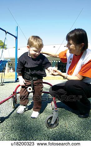 Stock Image - Adorable little boy with a disability learning to use a walker to get where he wants to go on the playground.. Fotosearch