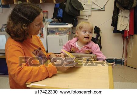 Stock Image - Adorable little girl with Down's Syndrome participating in occupational therapy with her teacher/therapist.. Fotosearch