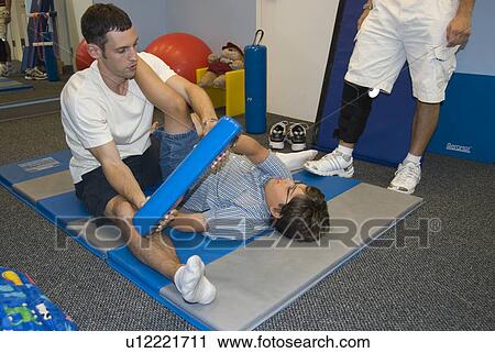 Boy with muscular dystrophy lays on a mat holding a blue bar as therapist stretches his left hamstring. View Large Photo Image Stock Image - Boy with muscular dystrophy lays on a mat holding a blue bar as therapist stretches his left hamstring.. Fotosearch