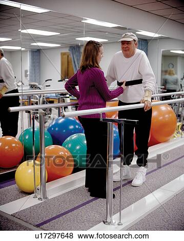 Elderly man with a disability receiving support from his physical therapist as he attempts to improve or maintain his ability to walk. View Large Photo Image Stock Photo - Elderly man with a disability receiving support from his physical therapist as he attempts to improve or maintain his ability to walk.. Fotosearch