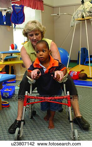 Stock Image - Little boy with multiple disabilities using a walker to increase his skills during a therapy session.. Fotosearch