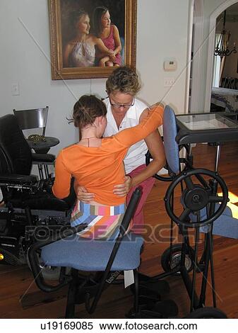 Mother helps daughter transfer from her wheelchair to a ôstanderö for a physical therapy session. View Large Photo Image Stock Photography - Mother helps daughter transfer from her wheelchair to a ôstanderö for a physical therapy session.. Fotosearch