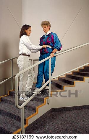 Woman with a disability receiving assistance in walking down the stairs during a session with her physical therapist. View Large Photo Image Stock Photo - Woman with a disability receiving assistance in walking down the stairs during a session with her physical therapist.. Fotosearch