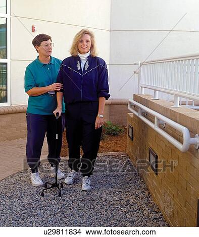 Woman with a disability relearning how to walk with the assistance of a therapist. View Large Photo Image Picture - Woman with a disability relearning how to walk with the assistance of a therapist.. Fotosearch