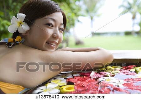 Stock Image - Young woman in a bath full of flowers, Saipan, Rear View. Fotosearch
