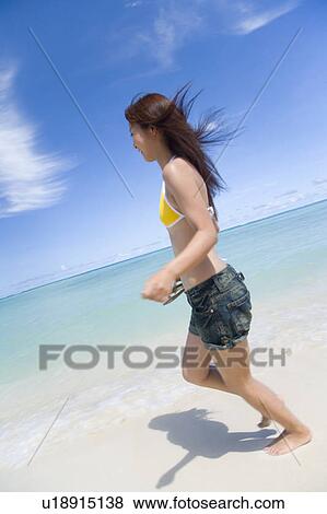 Stock Photo - Young woman running on beach, smiling, blurred motion, Saipan, USA . Fotosearch