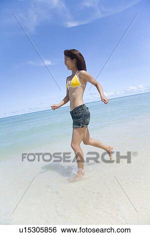 Stock Photograph - Young woman running on beach, smiling, Saipan, USA . Fotosearch