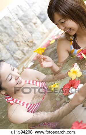 Stock Photo - Young women in a bath full of flowers, Saipan, Focus on Background. Fotosearch