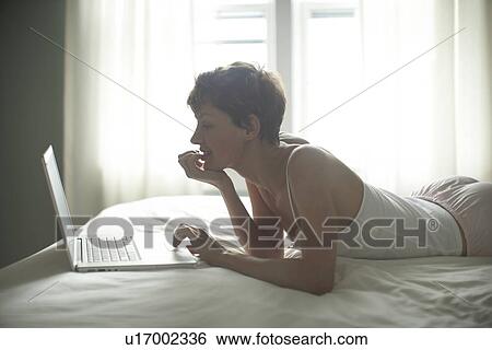 Mid adult woman using laptop on bed View Large Photo Image Stock Photograph - Mid adult woman using laptop on bed. Fotosearch