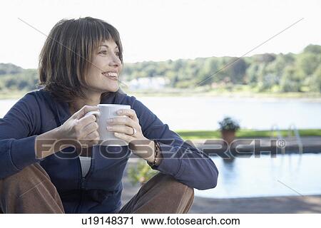 Stock Image - Woman drinking coffee by swimming pool. Fotosearch
