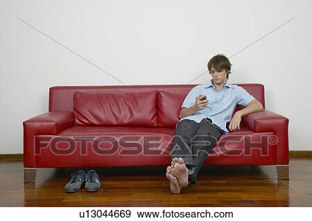 Young man looking at PDA on sofa View Large Photo Image Stock Photo - Young man looking at PDA on sofa. Fotosearch