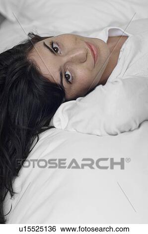 Stock Photograph - Young woman lying on bed (portrait). Fotosearch
