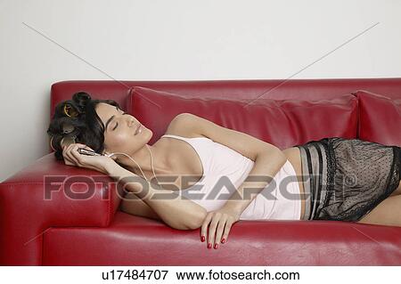 Stock Photo - Young woman lying on sofa and listening to MP3 player. Fotosearch