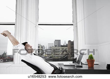 Stock Image - Businessman stretching at desk. Fotosearch
