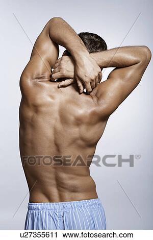 Stock Image - Mid adult man with hands behind head (rear view). Fotosearch