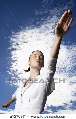 Picture - Young woman in hooded top with arms outstretched (low angle view). Fotosearch