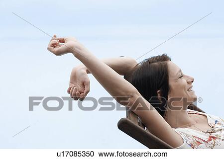 Stock Image - Young woman stretching on lounge chair. Fotosearch