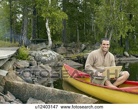 Man sitting in a boat with a laptop smiling. View Large Photo Image Stock Photo - Man sitting in a boat with a laptop smiling.. Fotosearch
