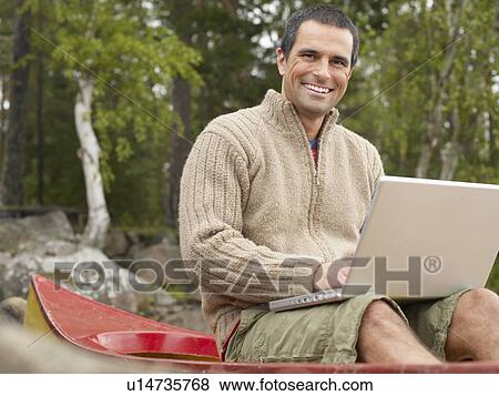 Man sitting in a boat with a laptop smiling. View Large Photo Image Stock Photo - Man sitting in a boat with a laptop smiling.. Fotosearch