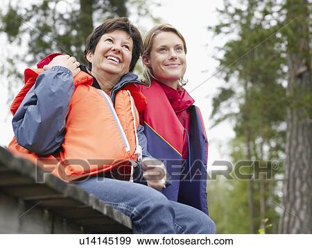 Stock Photo - Two women on a dock wearing life jackets smiling.. Fotosearch
