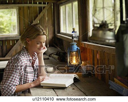 Woman sitting at a table in cabin with book smiling. View Large Photo Image Stock Image - Woman sitting at a table in cabin with book smiling.. Fotosearch
