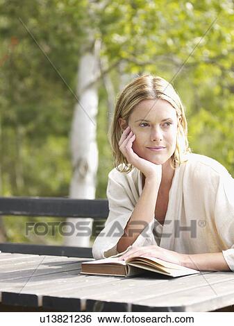 Woman sitting at a table outdoors with a book. View Large Photo Image Stock Photograph - Woman sitting at a table outdoors with a book.. Fotosearch