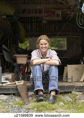 Stock Photo - Woman sitting in shed beside a saw smiling.. Fotosearch