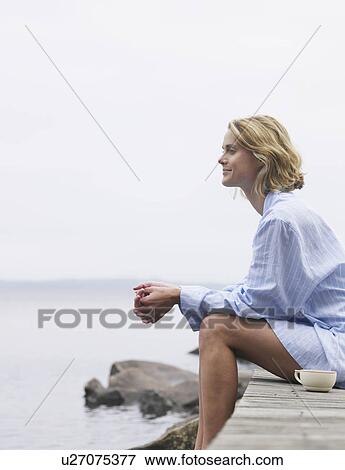 Stock Photo - Woman sitting on a dock with a mug.. Fotosearch