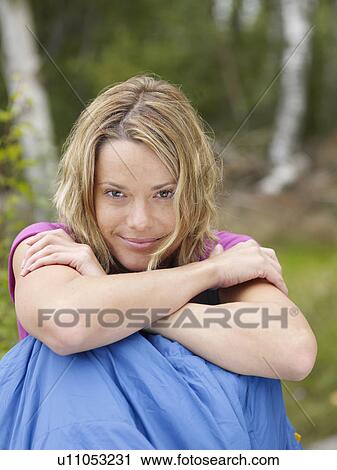 Stock Image - Woman sitting with a sleeping bag around waist smiling.. Fotosearch