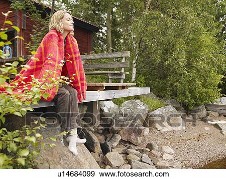 Stock Photo - Woman with blanket wrapped around her sitting on dock smiling.. Fotosearch