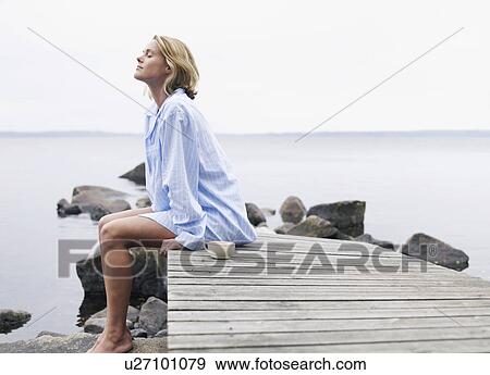 Woman with eyes closed sitting on a dock with a mug. View Large Photo Image Stock Photo - Woman with eyes closed sitting on a dock with a mug.. Fotosearch