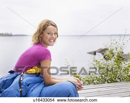 Woman with sleeping bag wrapped around her waist laughing by water. View Large Photo Image Picture - Woman with sleeping bag wrapped around her waist laughing by water.. Fotosearch