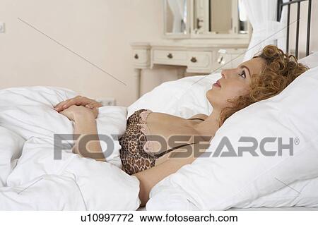 Stock Image - woman lying in bed looking up, side view, high section. Fotosearch